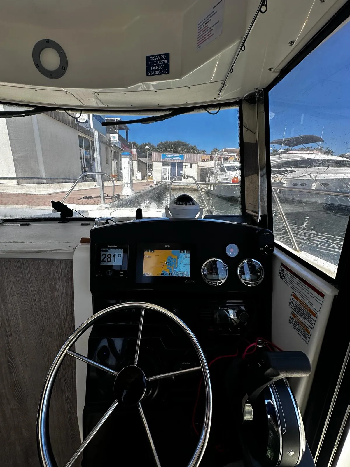 Timonerie d'un bateau avec tableau de bord, compas de route, GPS et vue sur le port de plaisance d'Hyères